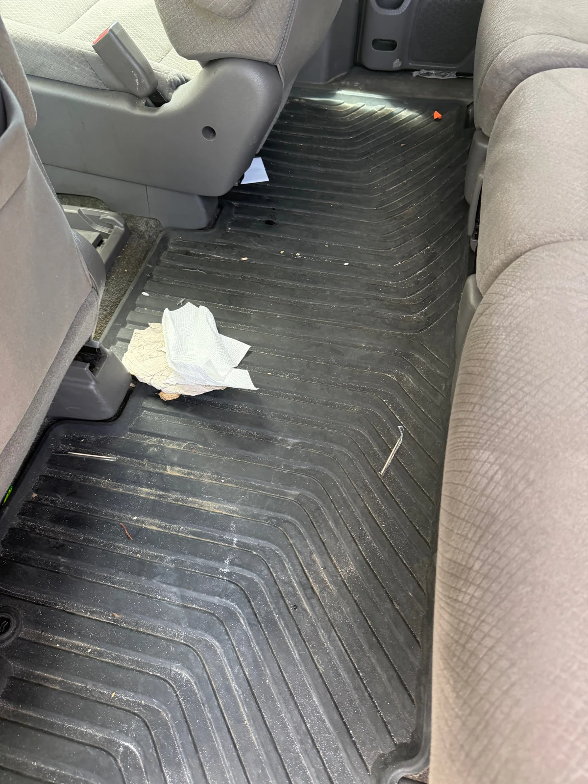 Honda Odyssey second-row floor before detailing, with trash and debris on the rubber mat